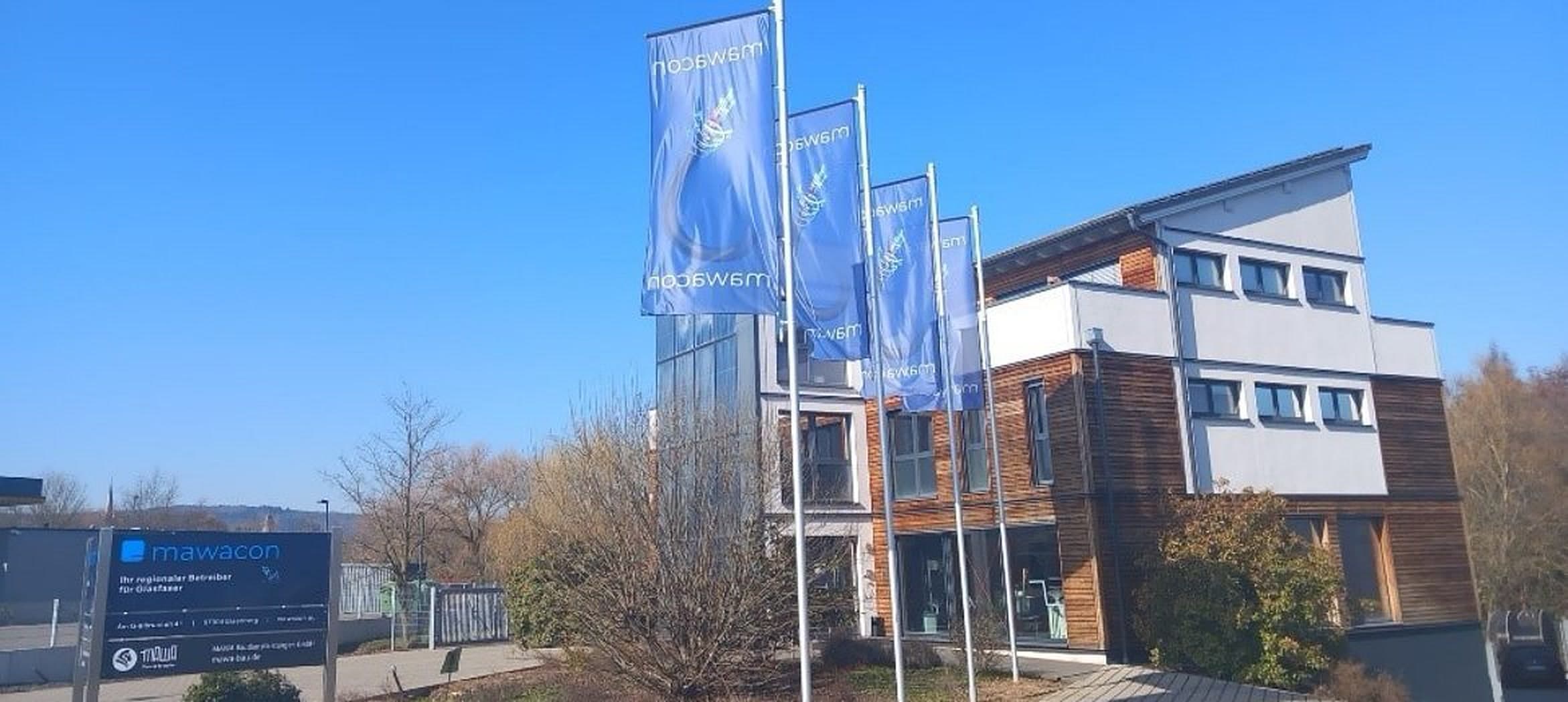 Mawacon Hauptsitz in Eisenberg mit Firmenflaggen und Glasfaser-Beschilderung